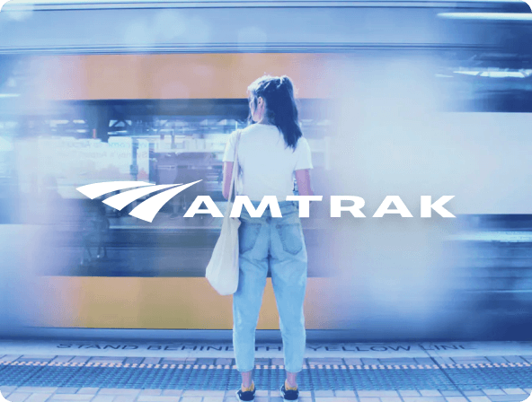 Woman standing in front of passing train with amtrak logo in front.  Themed blue.